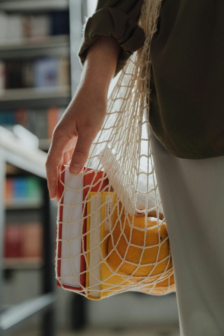 Close-up of a woman holding a string bag with groceries and books, promoting zero waste lifestyle.