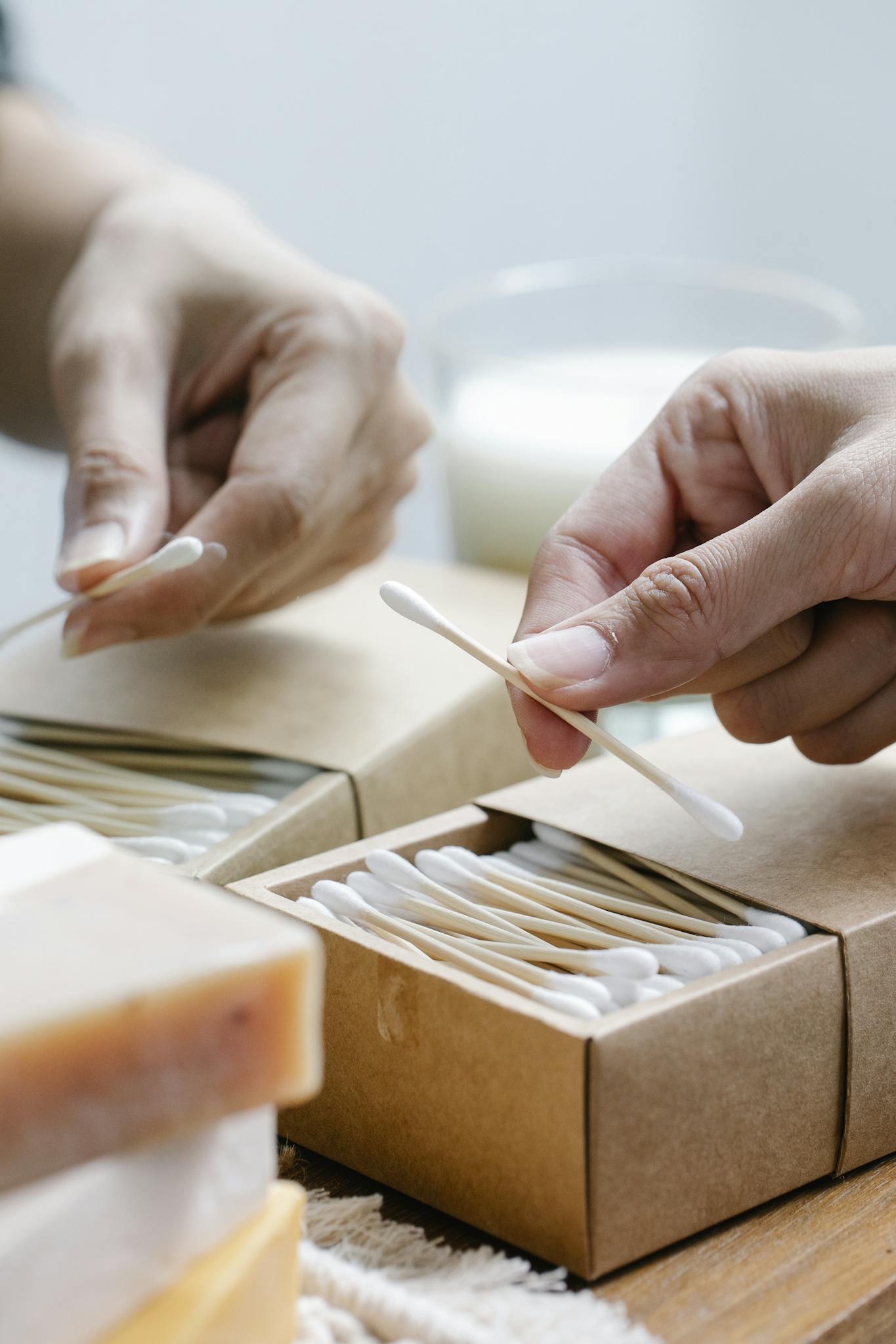 Close-up of hands using eco-friendly cotton swabs in cardboard packaging.